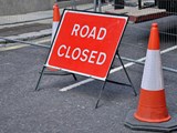 picture of a tarmac road with orange cones and a red road closed sign